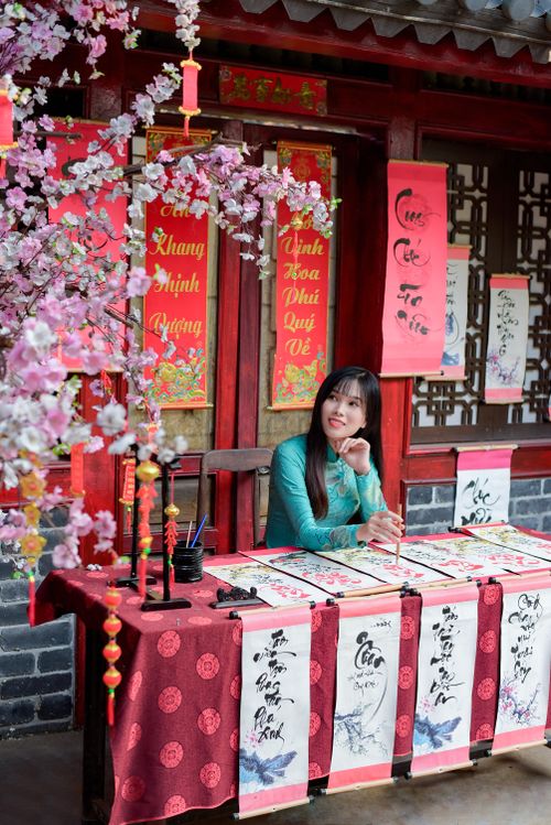 Free Woman in traditional attire practicing calligraphy amidst cherry blossoms in a vibrant cultural setting. Stock Photo