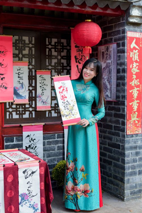 Free Young woman in ao dai holding painting in festive setting, smiling. Stock Photo