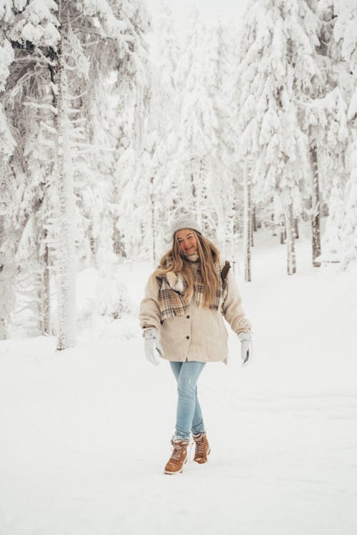 A Woman in Winter Clothes Standing on Snow Covered Ground in the Forest