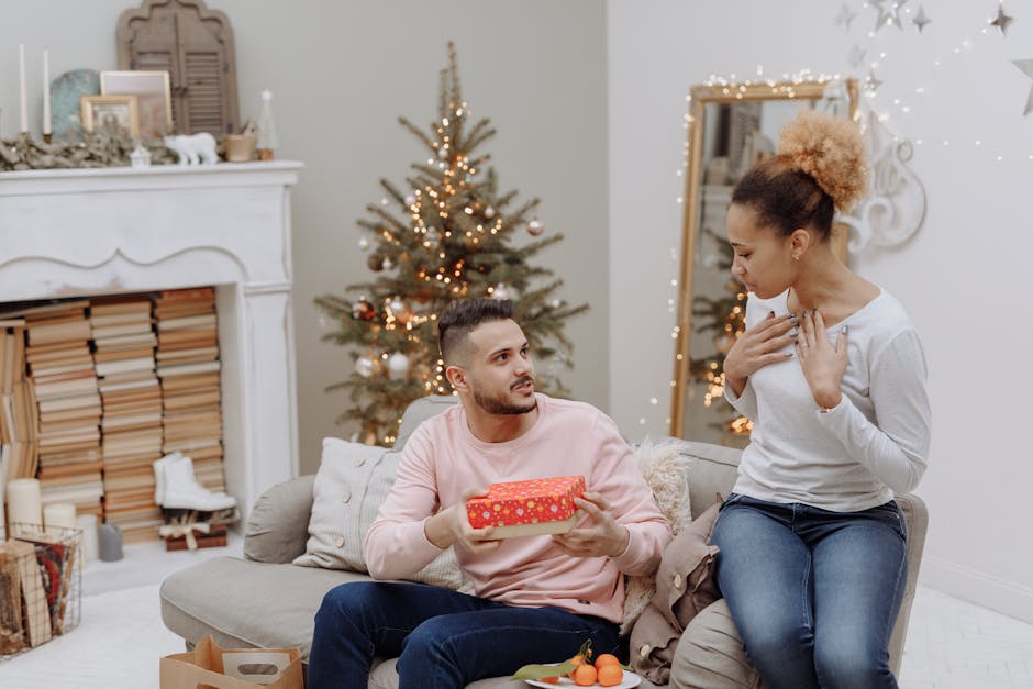 A man and woman sharing a special moment with a gift beside a Christmas tree indoors.