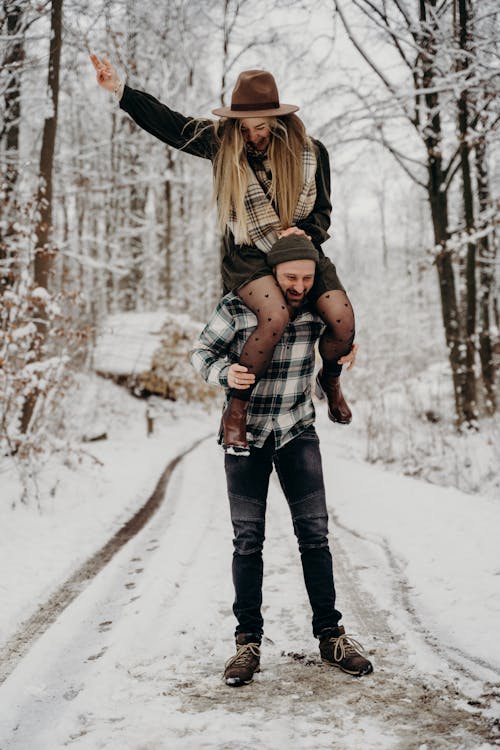A Man Carrying a Woman on his Shoulders in the Middle of a Snow Covered Road