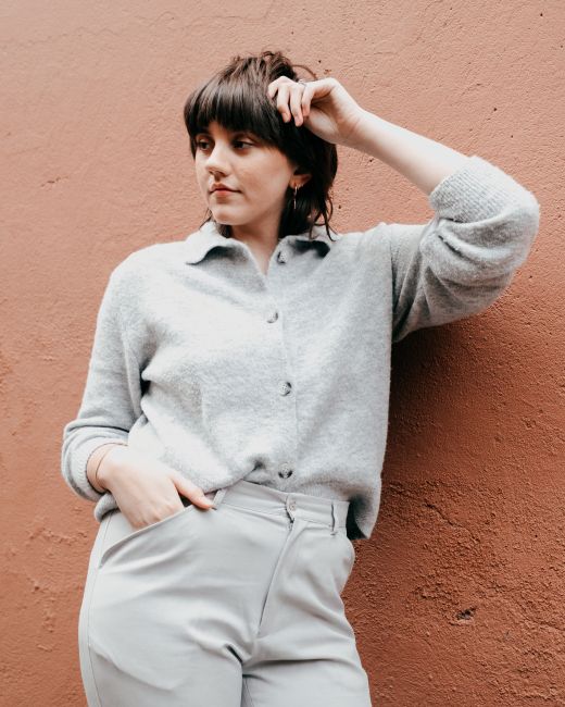 Pensive young female with hairstyle in casual clothes standing with hand in pocket and raised arm near concrete wall and looking away in daylight