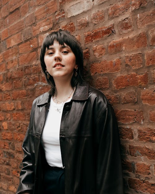 Charming female in leather jacket standing near brick wall