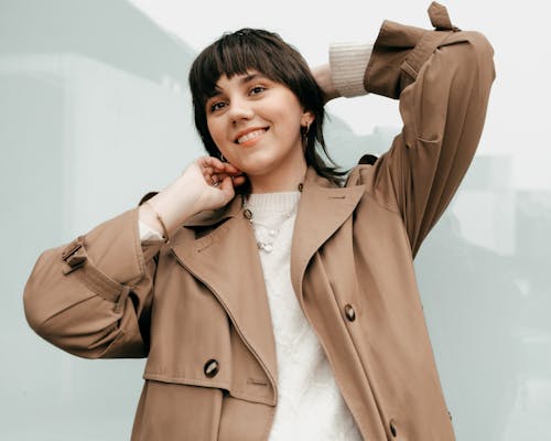 Smiling female in trendy coat standing with raised hands