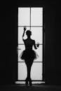 Black and white back view of anonymous female ballet artist silhouette standing on tiptoes against door