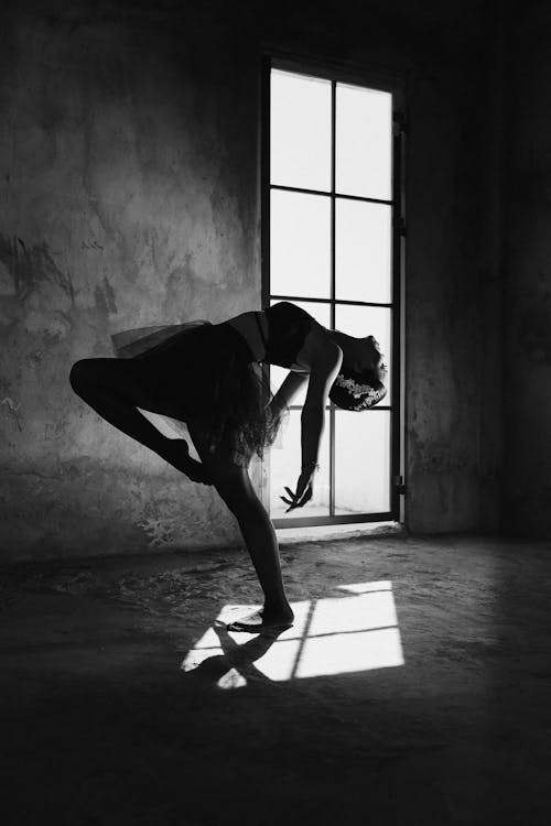 Graceful ballerina dancing in house with shadow on floor