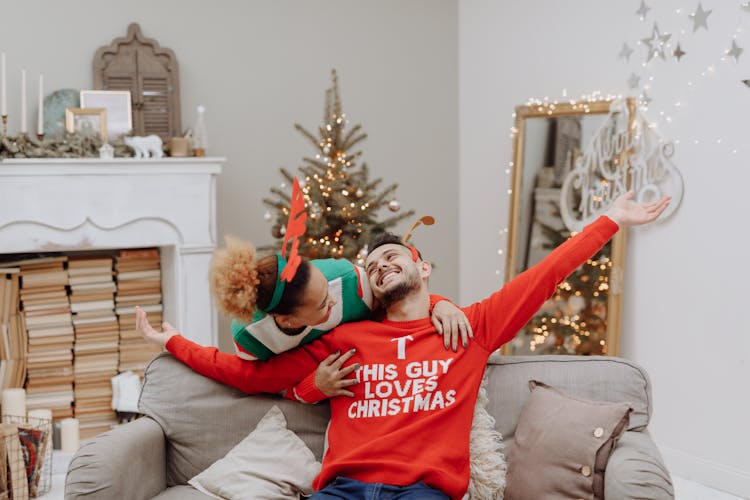 A Woman Hugging A Man In Ugly Christmas Sweater Sitting On Sofa