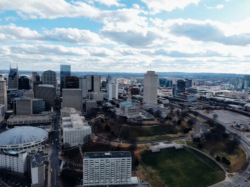 Drone view of modern multistory building exteriors and trees under cloudy sky in town