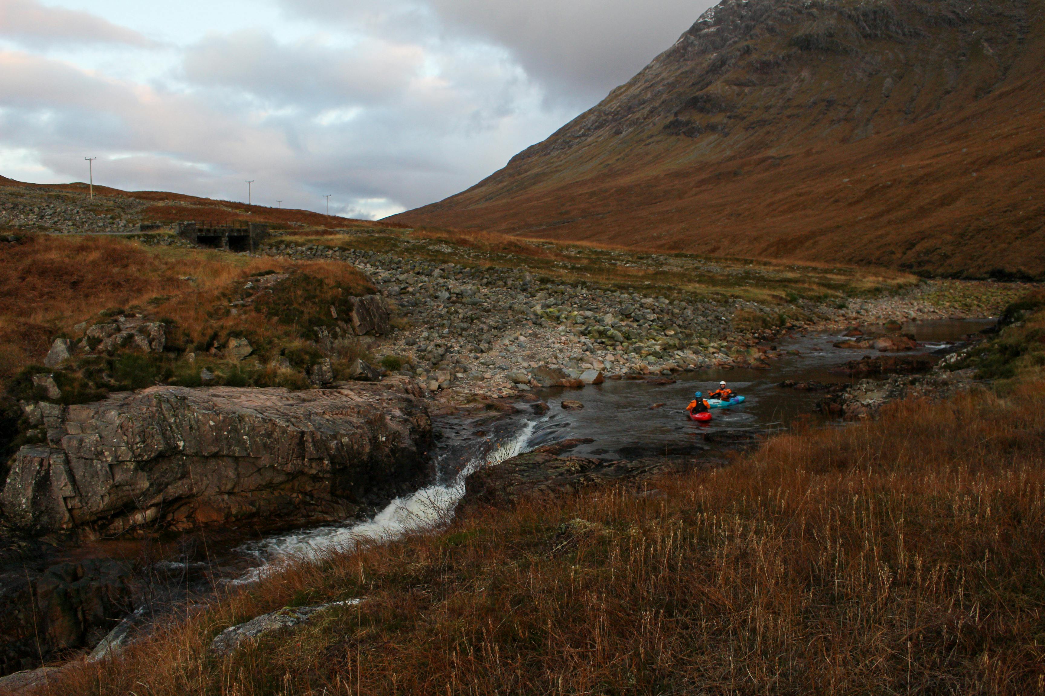Two kayakers navigate a serene river in Scotland's breathtaking highlands during autumn.