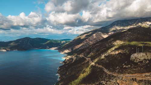 Free Stunning aerial shot of a rugged mountain coastline against a clear blue sea under dramatic clouds. Stock Photo