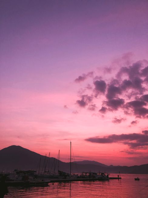 Peaceful sunset at Fethiye Marina, capturing vibrant pink and purple skies over silhouetted boats and mountains.
