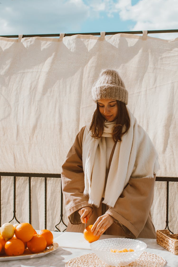 A Woman In Winter Clothes Slicing An Orange Fruit