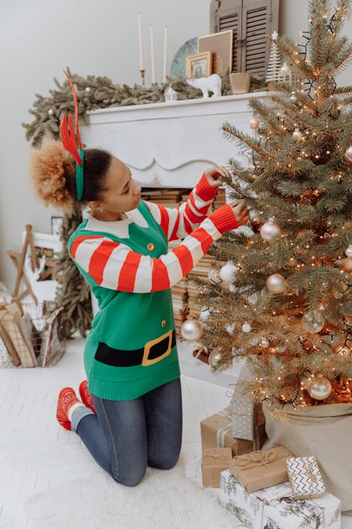 Woman in Green Red and White Sweater Decorating the Christmas Tree