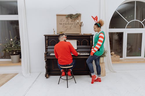 Free A Man Playing the Piano Near a Woman with a Reindeer Headband Stock Photo