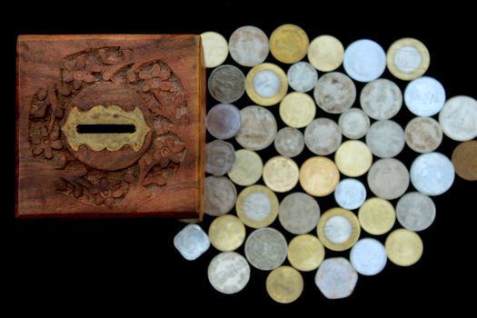 Top view of a vintage wooden piggy bank and assorted coins on a black surface, symbolizing savings and wealth.