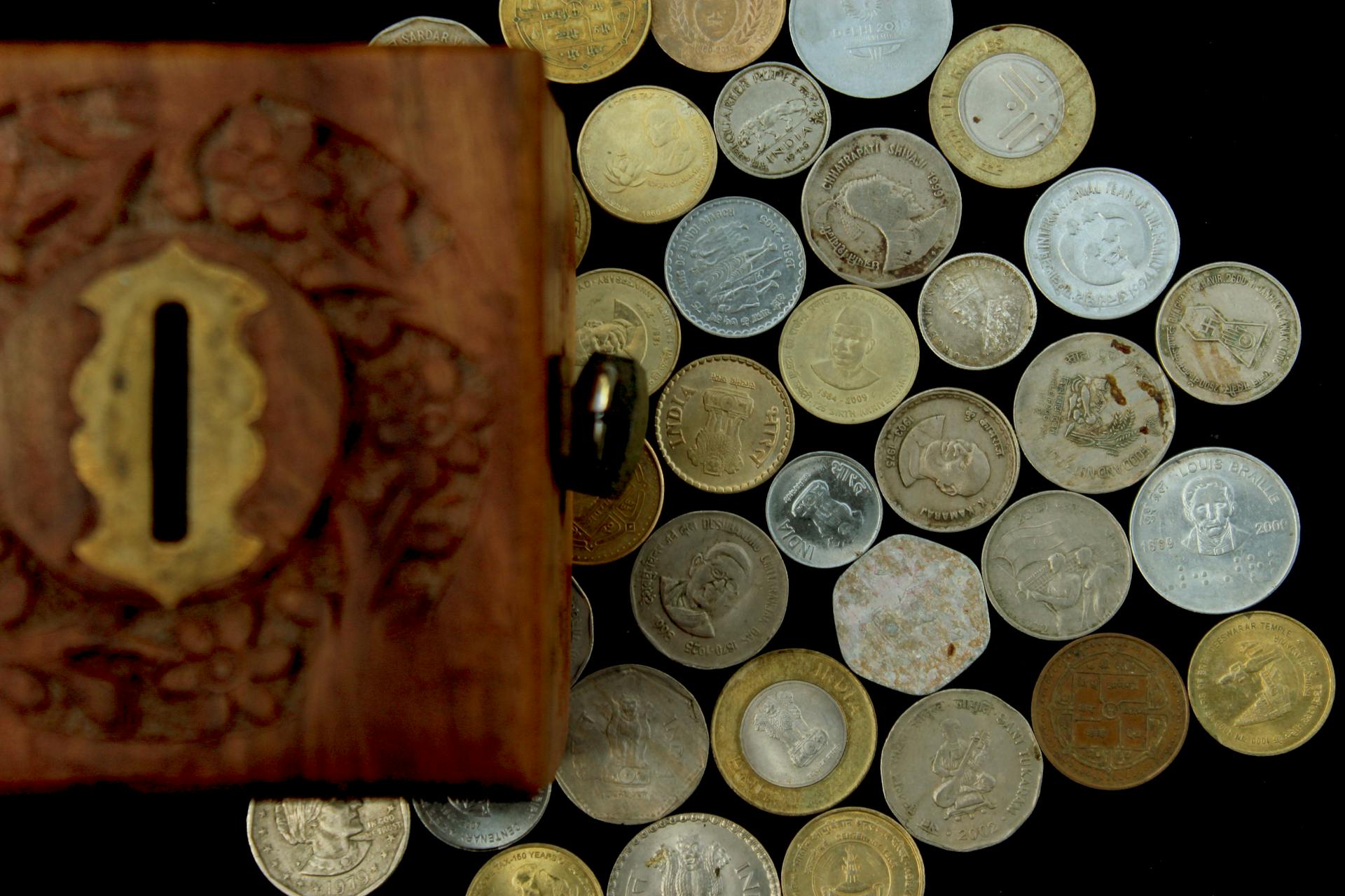 Collection of various Indian coins displayed with a carved wooden savings box.