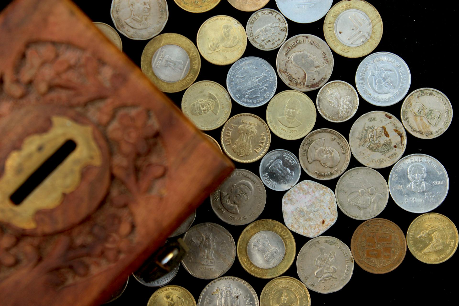 A diverse set of Indian coins displayed with an intricately carved wooden box, perfect for financial and cultural themes.