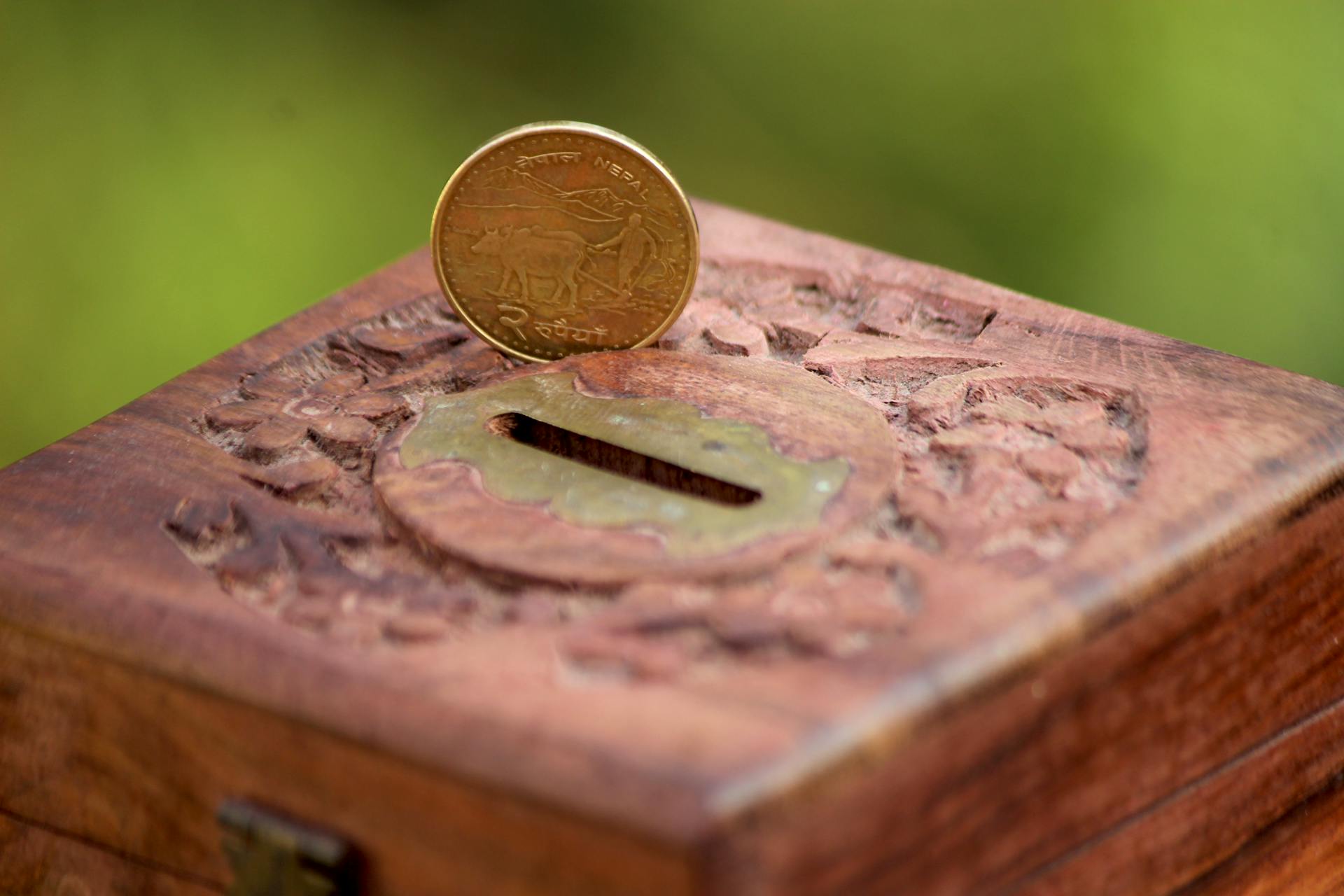 Detailed shot of a wooden savings box with an Indian coin, symbolizing wealth and investment.