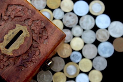 Beautifully carved wooden coin box surrounded by assorted coins, showcasing Indian craftsmanship.
