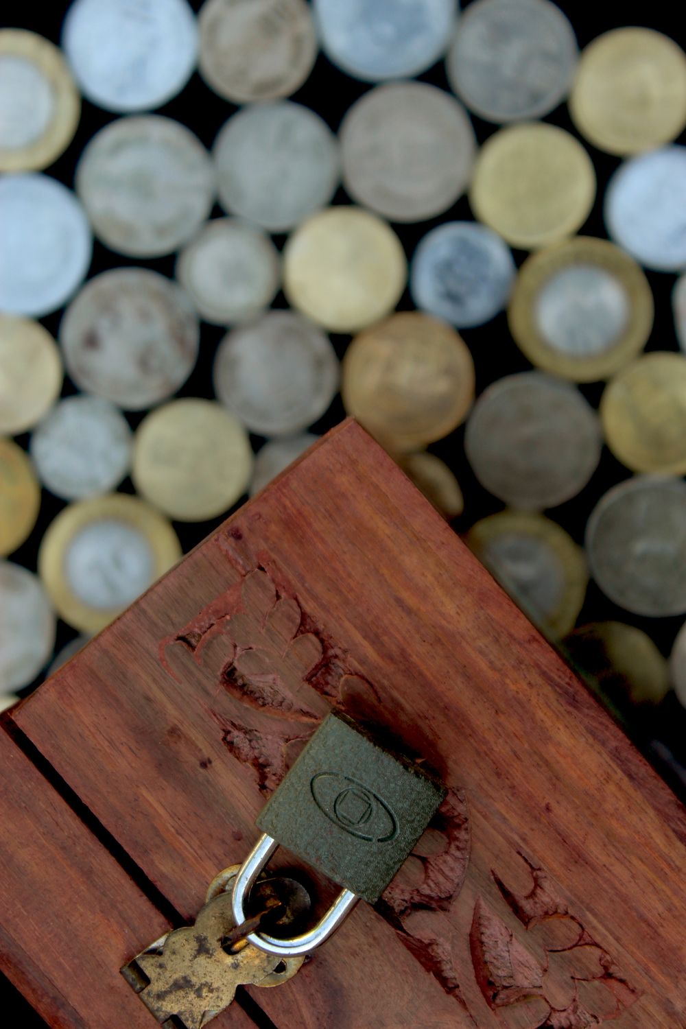 Locked wooden savings box surrounded by coins, representing financial protection