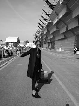 在意大利费拉拉，一位优雅的女子拿着购物袋，在现代建筑旁摆姿势