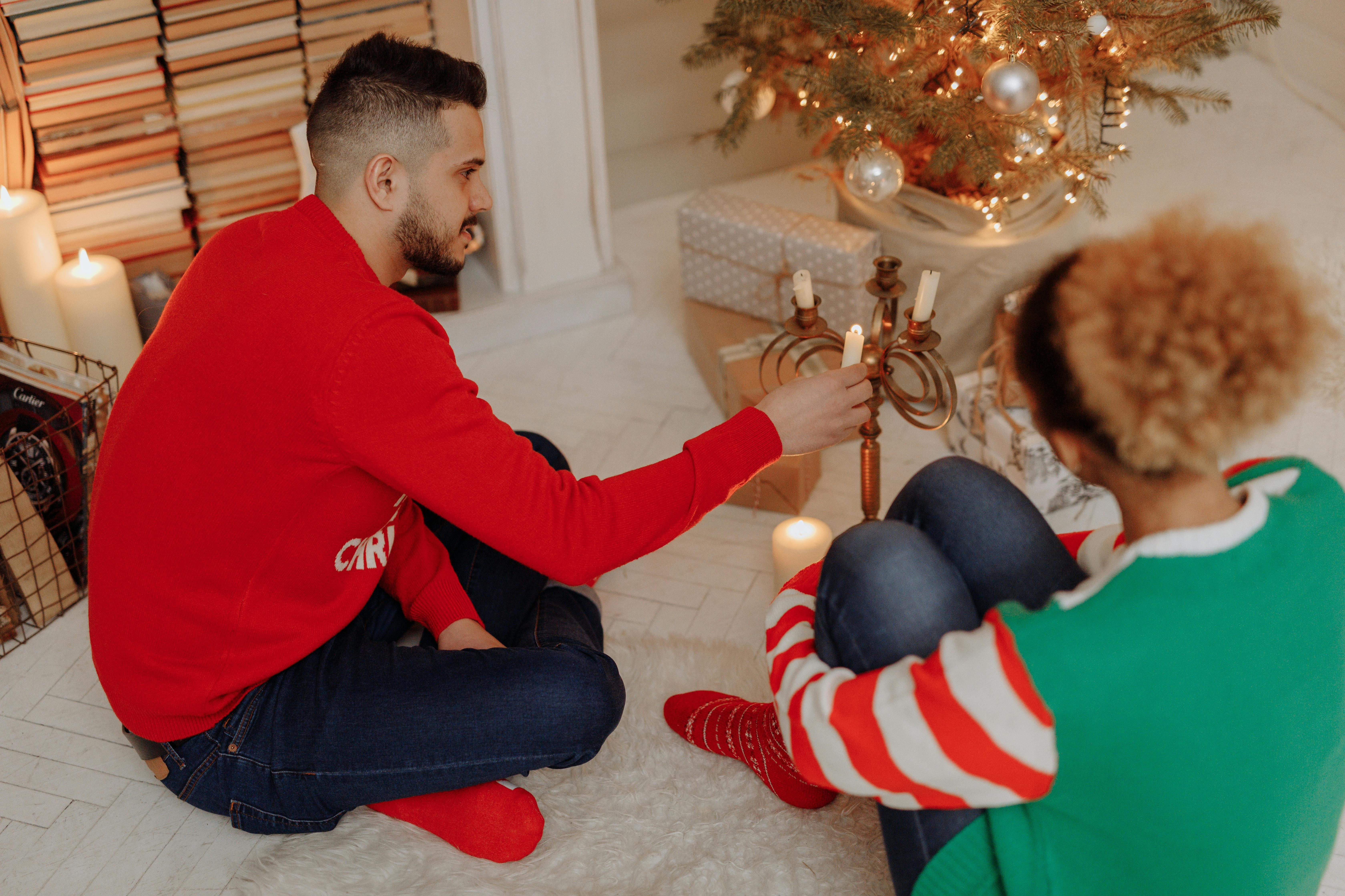 Two people sitting by a Christmas tree lighting candles, creating a cozy holiday atmosphere.
