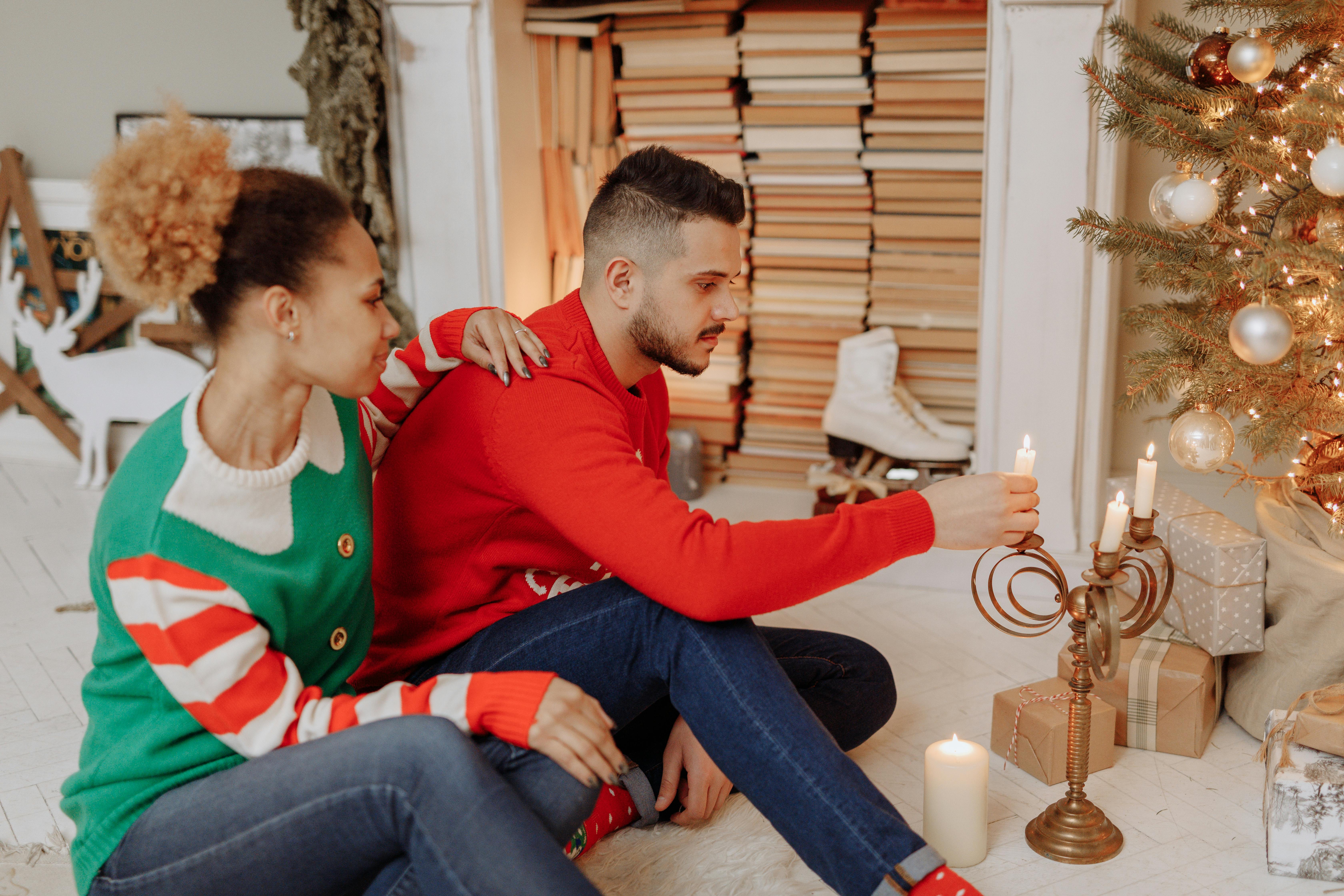 Couple celebrating Christmas at home, lighting candles near a decorated tree. Warm holiday ambiance.