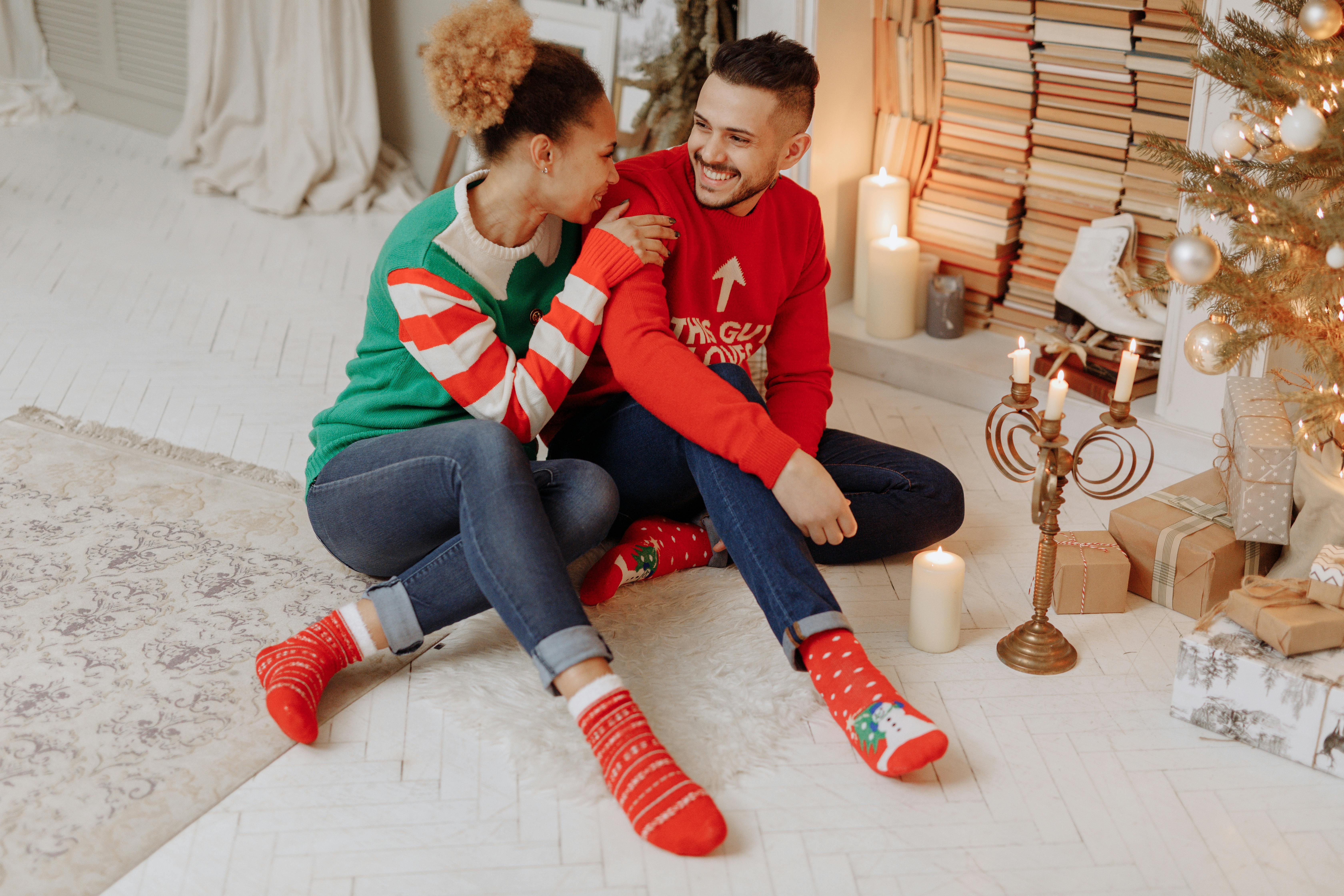 Smiling couple enjoying the holiday season by the Christmas tree with warm candles and cheerful decorations.