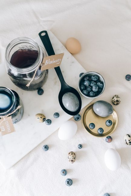 Flat lay of Easter eggs dyed with blueberries, featuring jars, spoons, and eggs on a table.