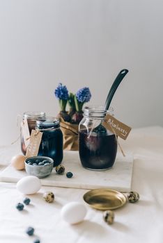 Glass jars with blueberry dye for Easter eggs alongside fresh flowers and eggs.