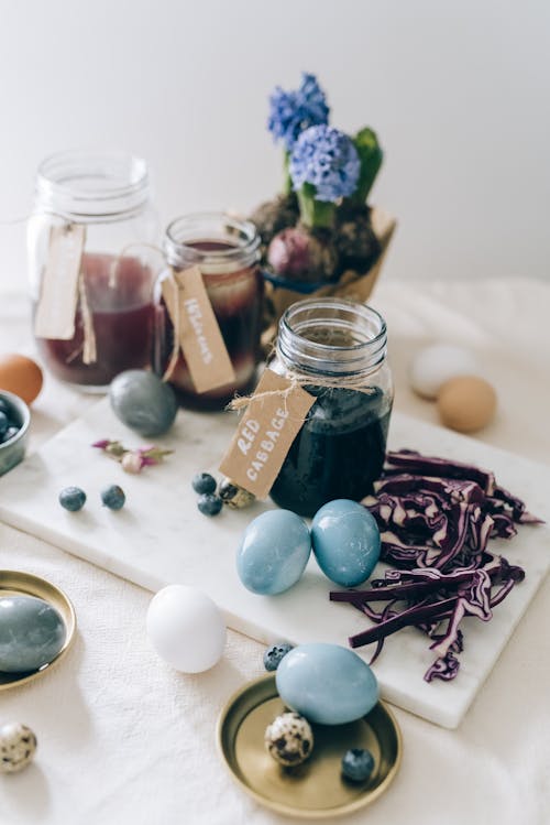 Glass Jars With Colored Liquids And Blue Eggs On Table