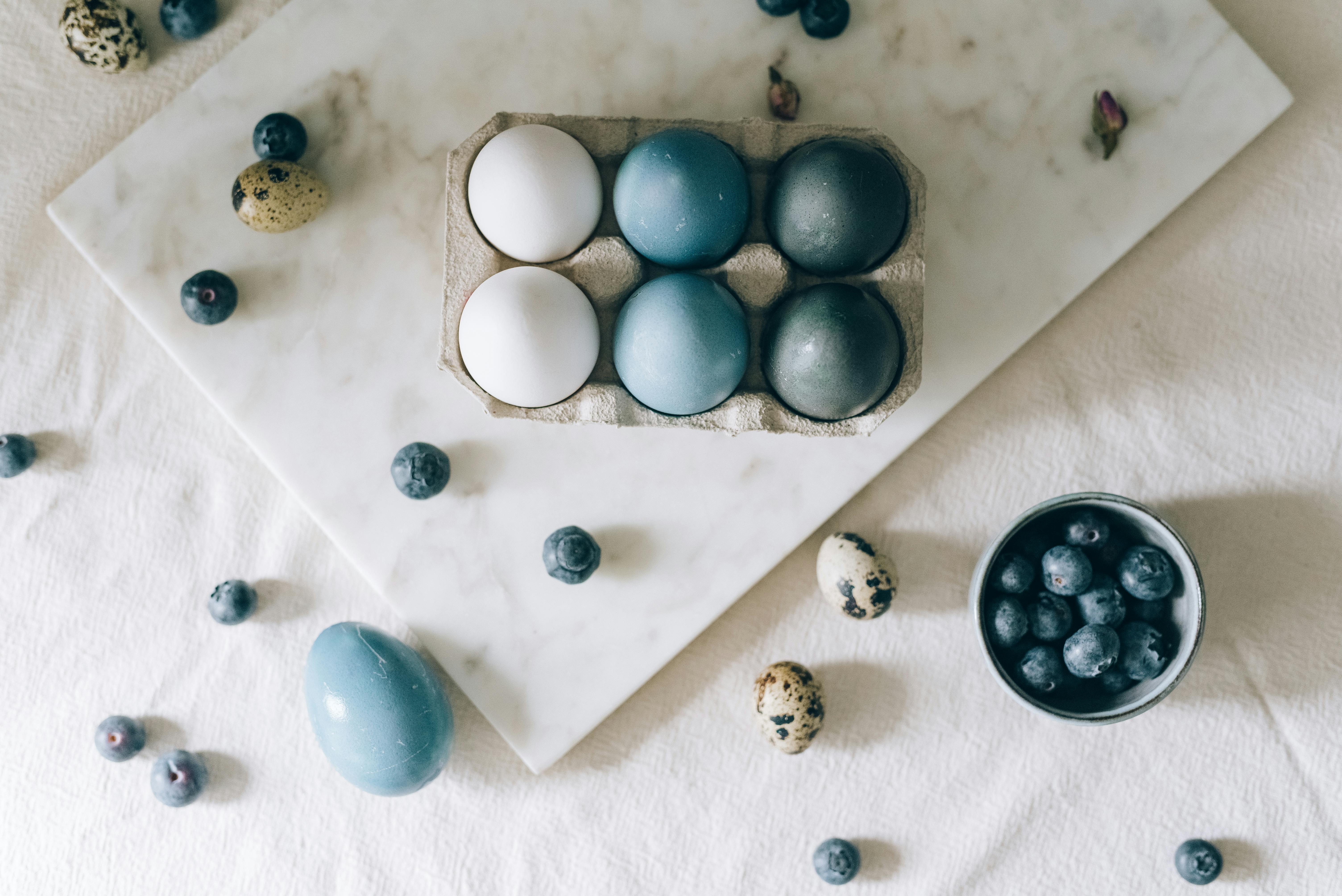 Top view of naturally dyed Easter eggs with blueberries on a marble surface, offering an elegant and creative still life composition.