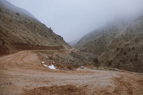 Free A foggy mountain road curves through rugged terrain with a single vehicle visible, offering a remote wilderness view. Stock Photo
