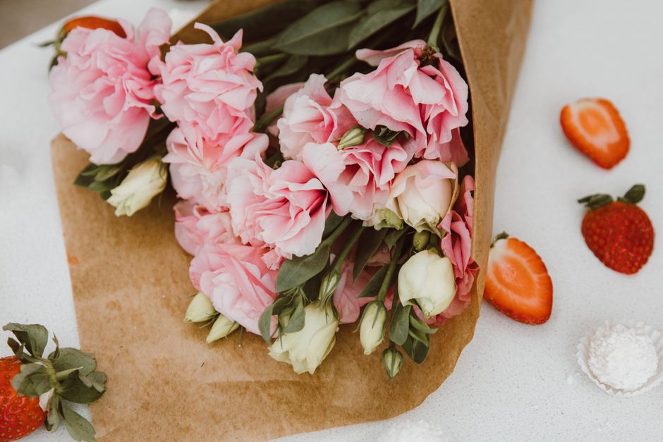 A beautifully arranged bouquet of pink and white flowers wrapped in brown paper with strawberries.