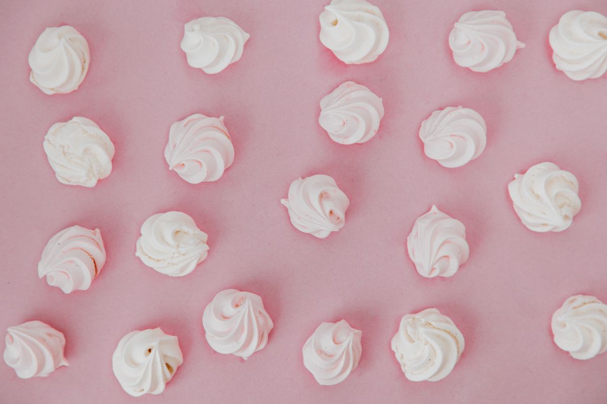 A collection of pink and white meringues arranged on a pastel pink surface, showcasing a sweet and elegant dessert.