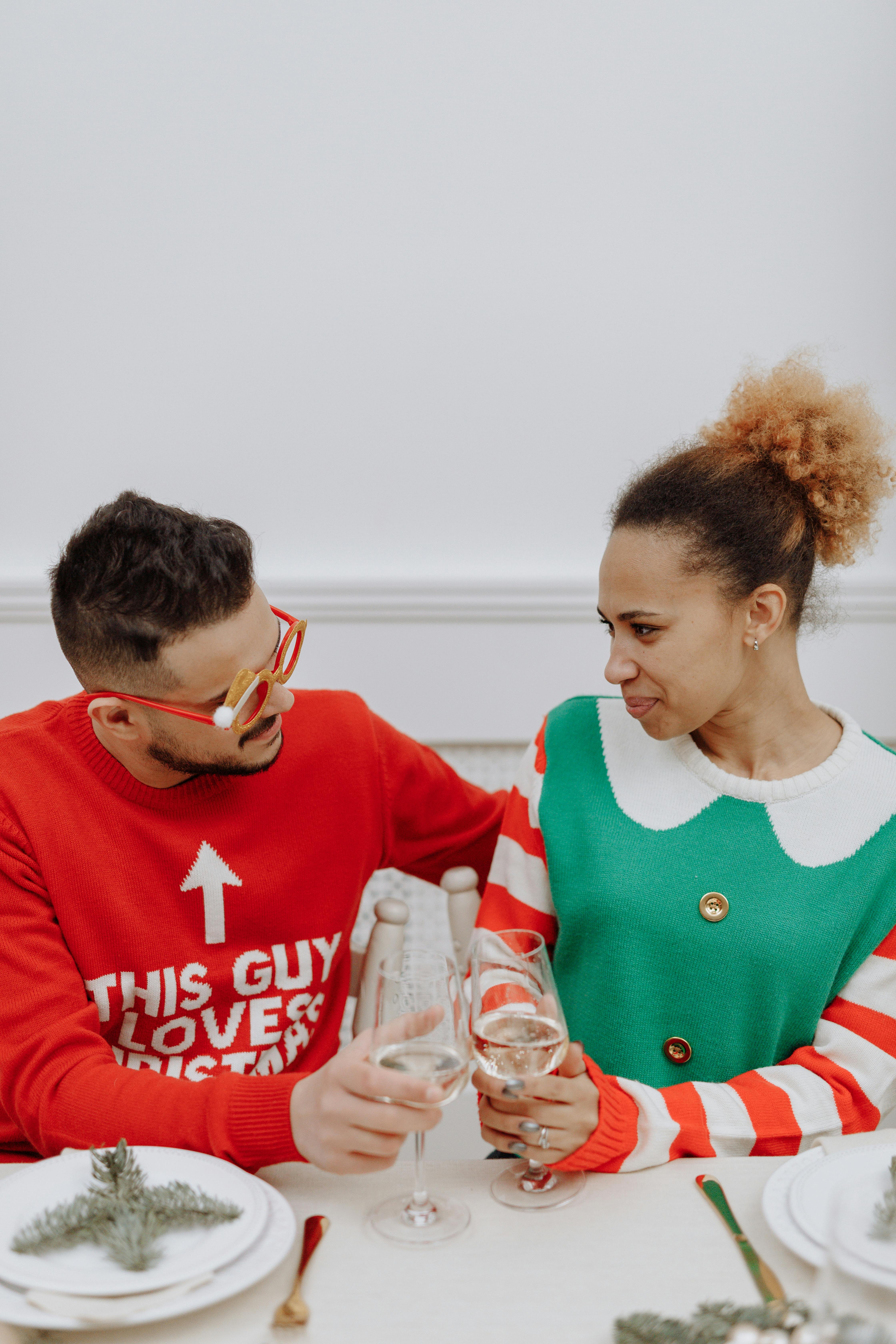 A cheerful couple celebrates with a toast in Christmas sweaters, spreading holiday cheer indoors.