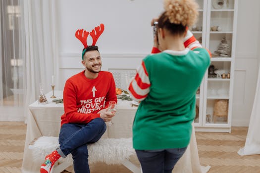 A joyful couple in festive sweaters capturing Christmas moments indoors with holiday decor.