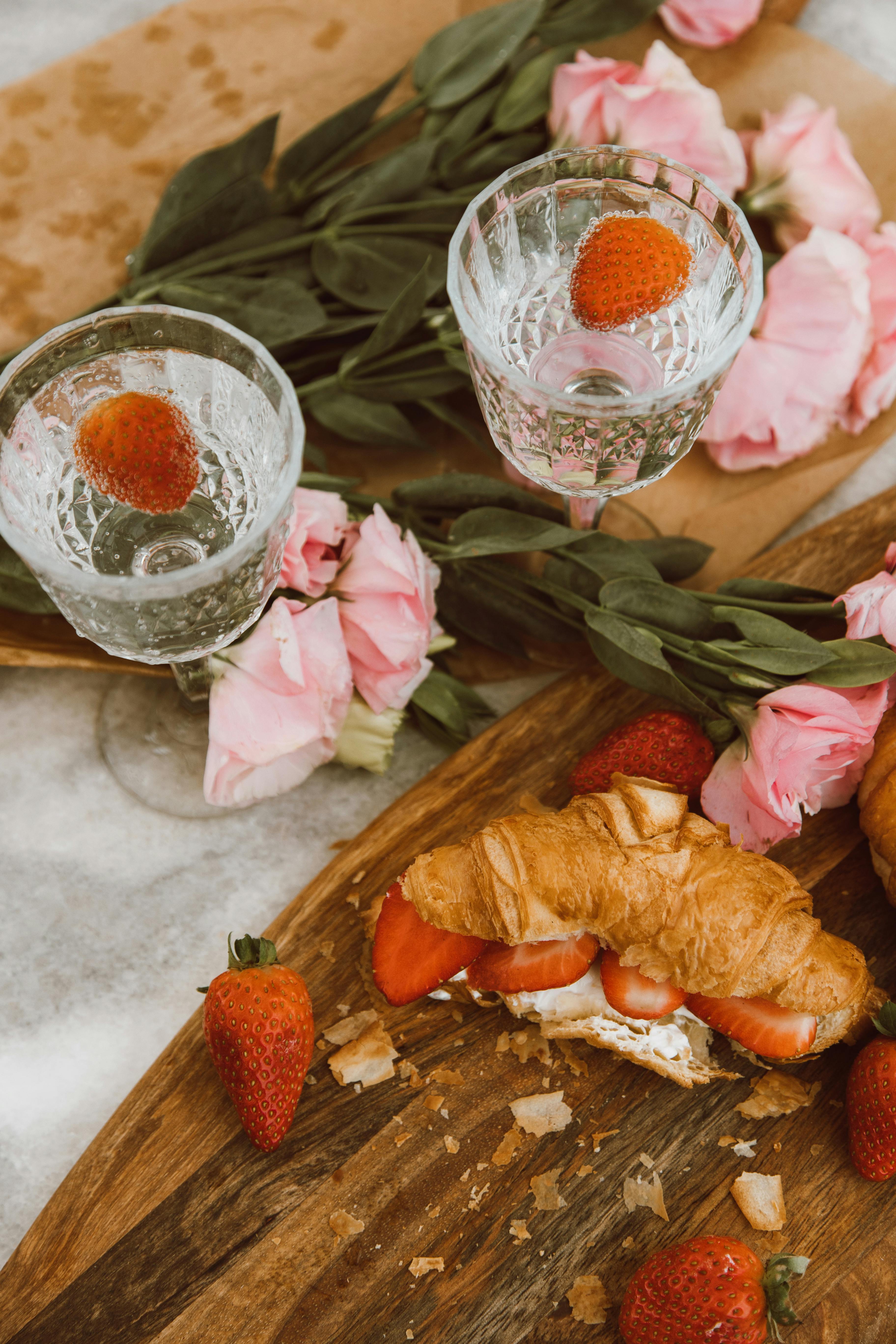 Flat lay of a picnic setup with croissants, strawberries, and pink flowers, creating a French elegance.