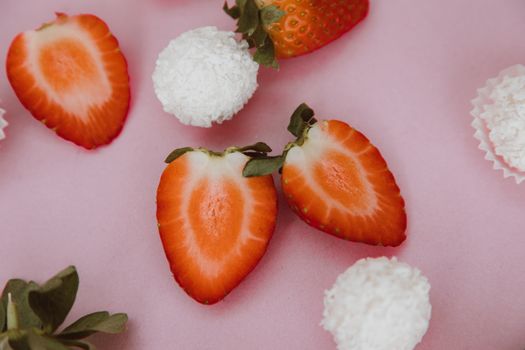 Close-up of fresh strawberry halves and coconut sweets on a pink background.