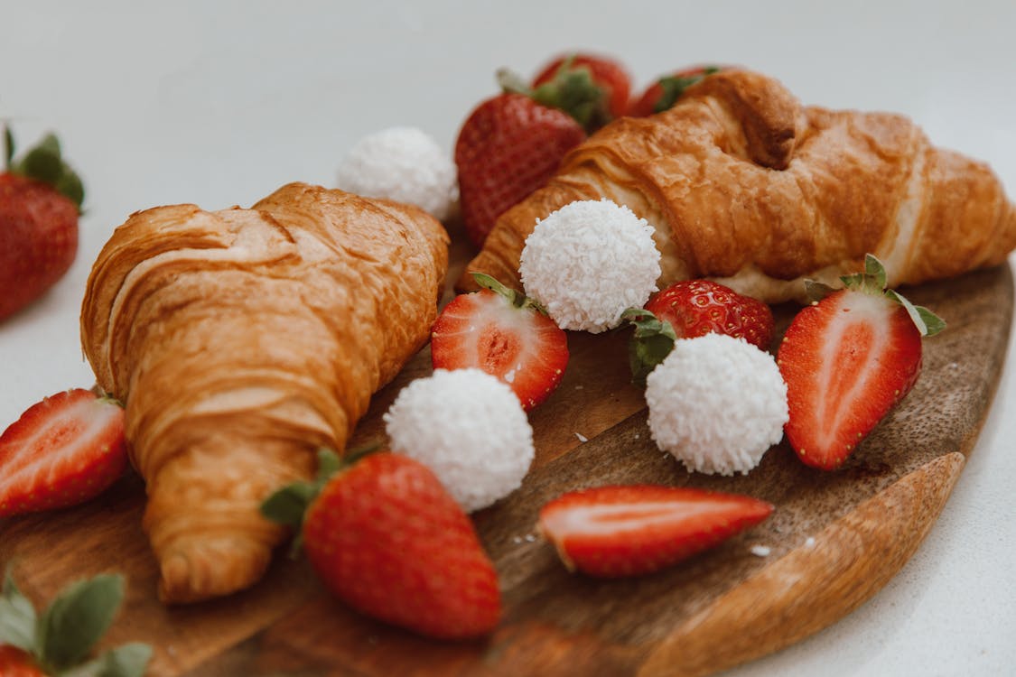 A Pair of Croissants with Slices of Strawberries and Sugar Balls on a Wooden Board