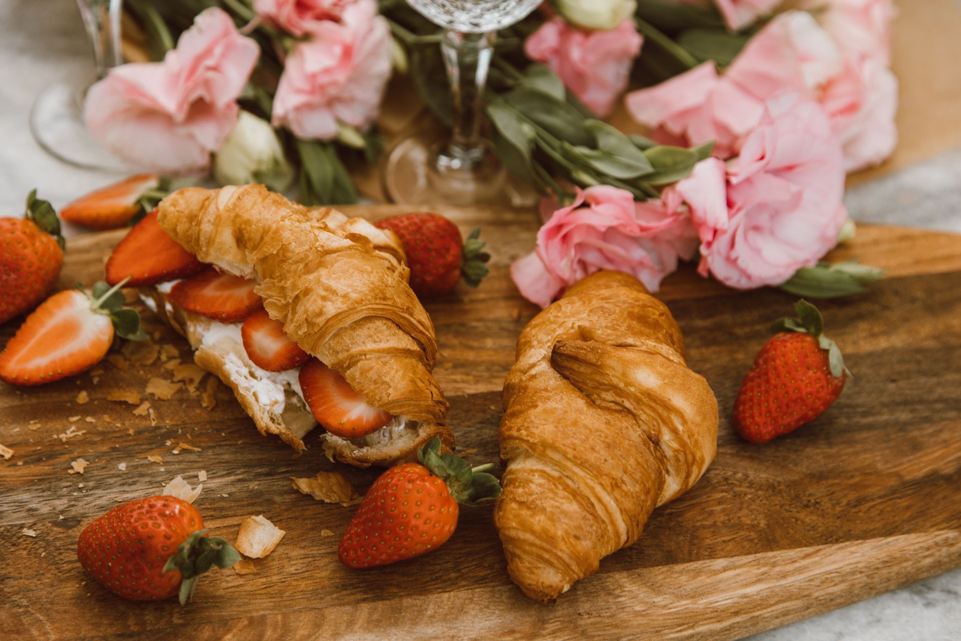 Elegant still life featuring croissants, strawberries, and pink roses on a wooden board.