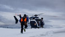 A Man in Reflective Jacket Running Towards a Helicopter on Snow Covered Ground