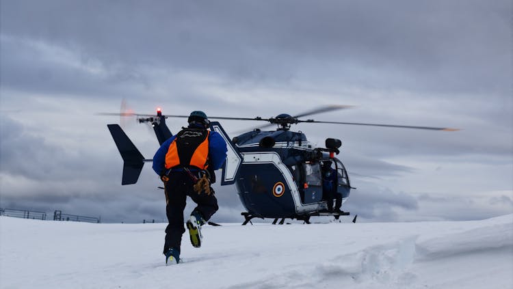 A Man In Reflective Jacket Running Towards A Helicopter On Snow Covered Ground