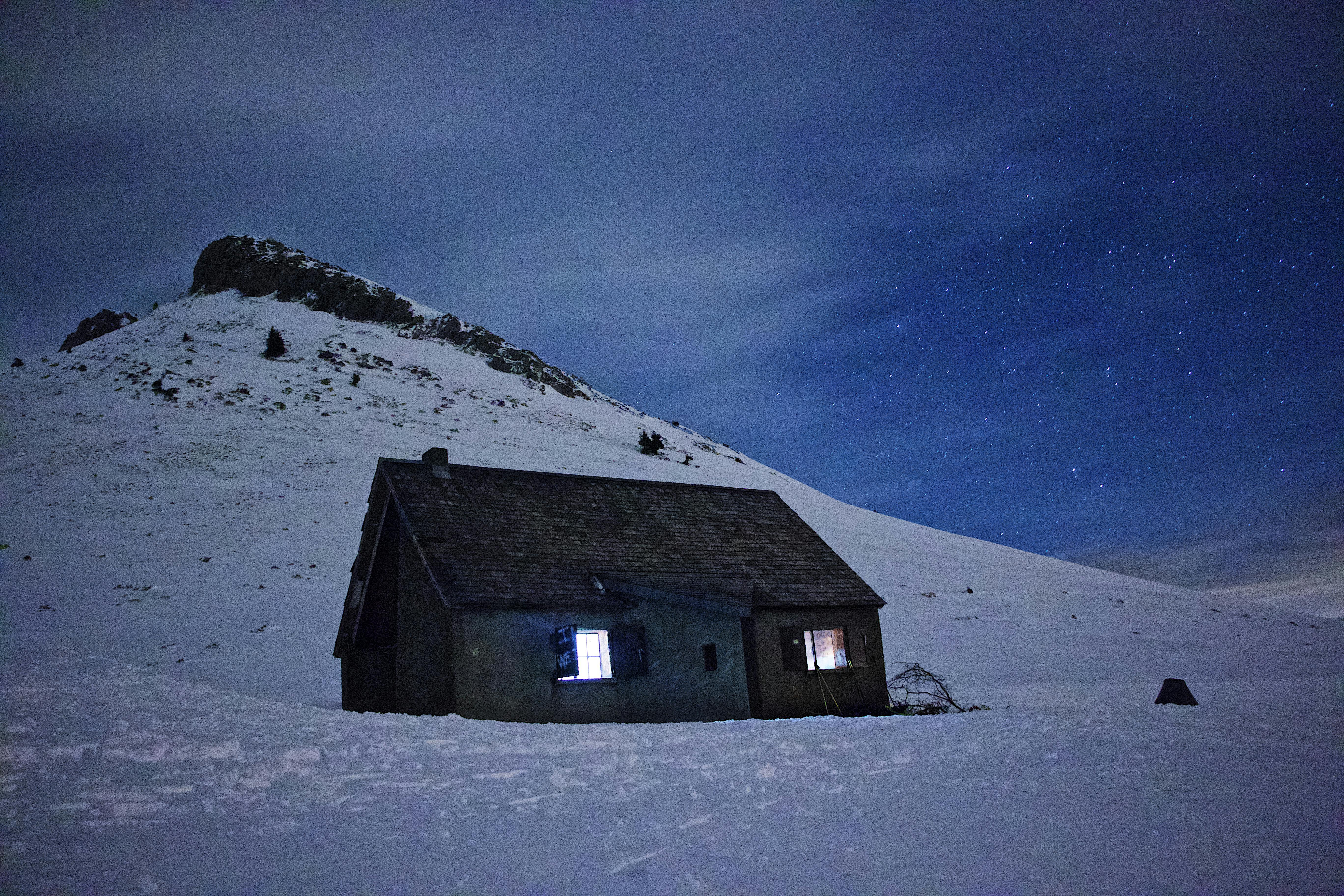 A cozy cabin nestled in a snowy mountain landscape under a clear, starry night sky.