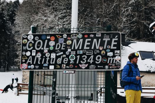 Sign at Col de Menté mountain pass surrounded by snowy trees and winter scenery.