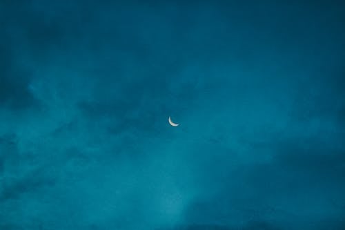 Free From below of crescent moon shining high in air on dark sky with clouds in evening time in nature at sunset Stock Photo