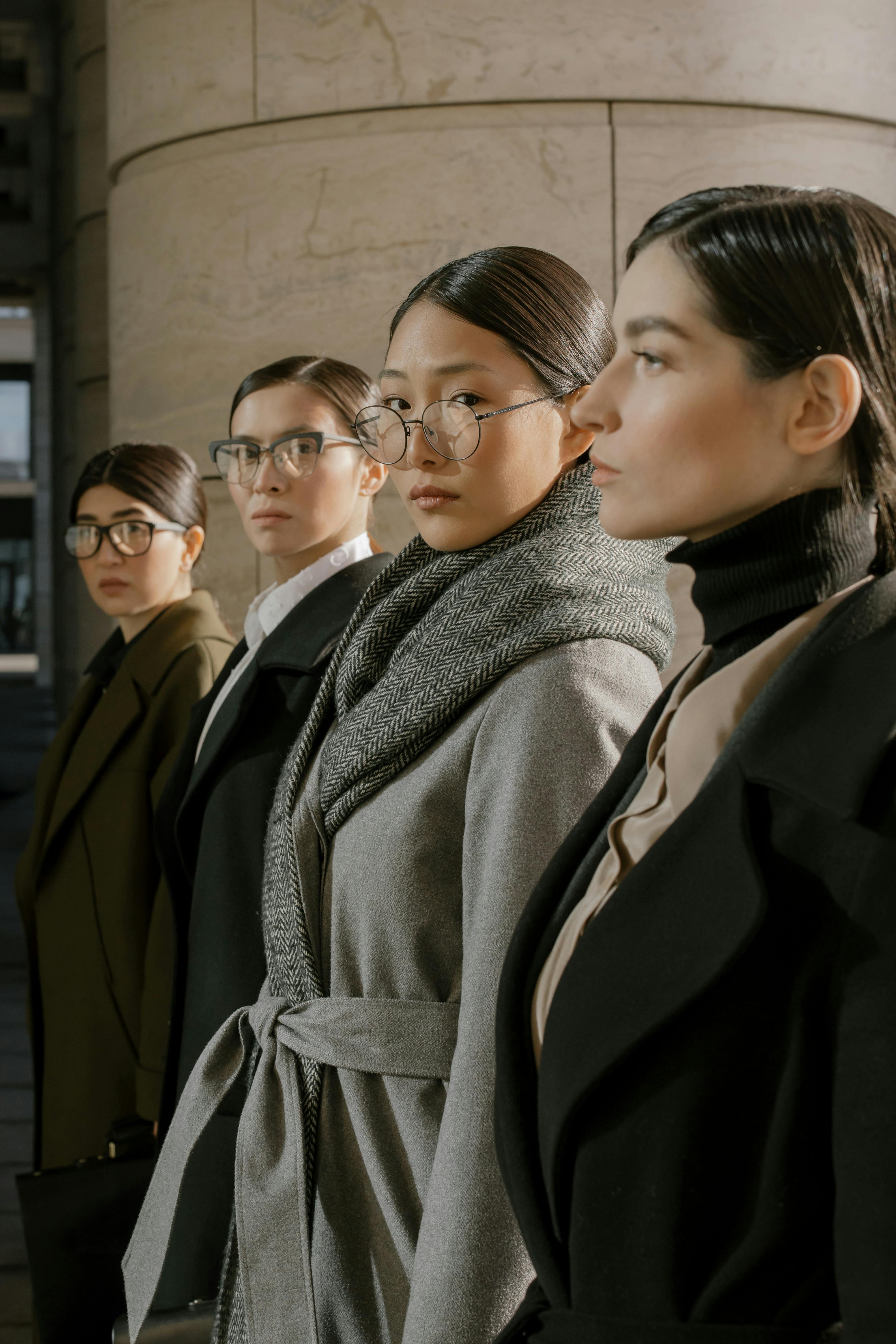 Group of diverse women in fashionable coats and glasses exuding confidence and style.