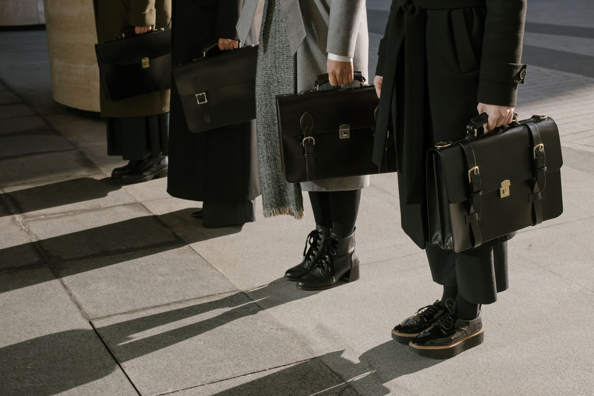 Row of business professionals holding leather briefcases outdoors.