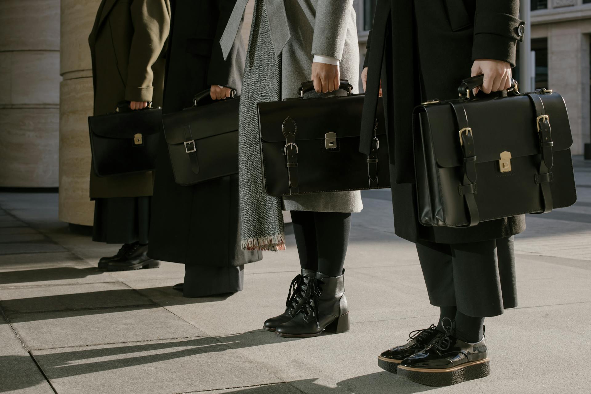 Three professionals stand with leather briefcases, illustrating business style.