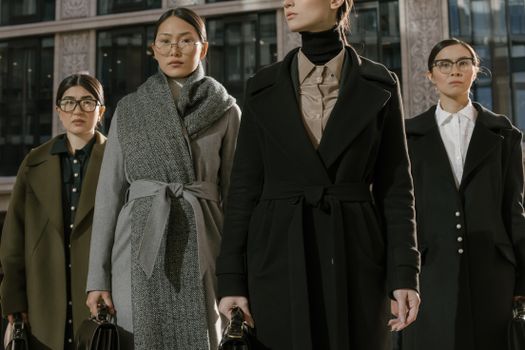 A group of fashionable women in coats standing confidently in an urban environment.